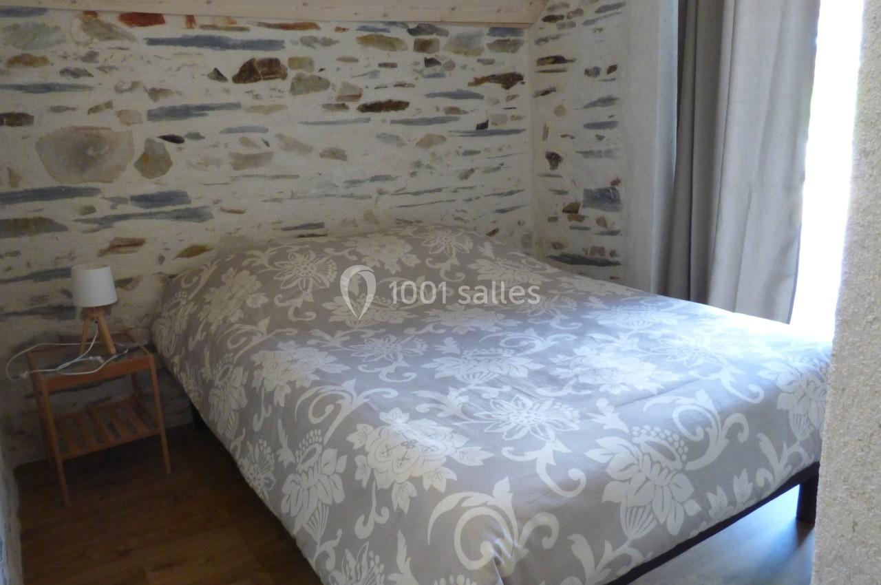 Chambre mansardée avec murs en pierre, lit double couvert d'une housse à motifs floraux, parquet et lumière naturelle.