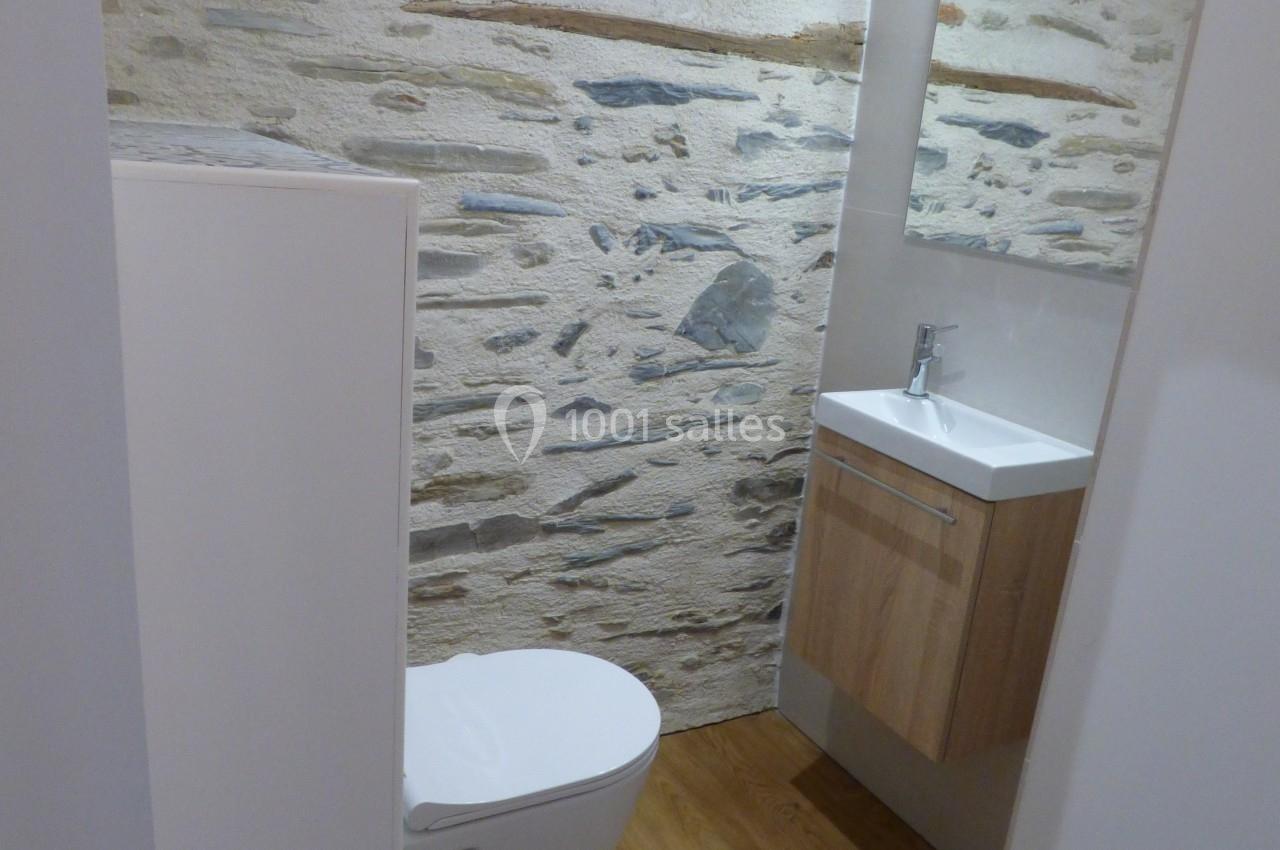 Toilettes modernes avec mur en pierre apparente, sol en bois, lavabo suspendu et miroir éclairé.