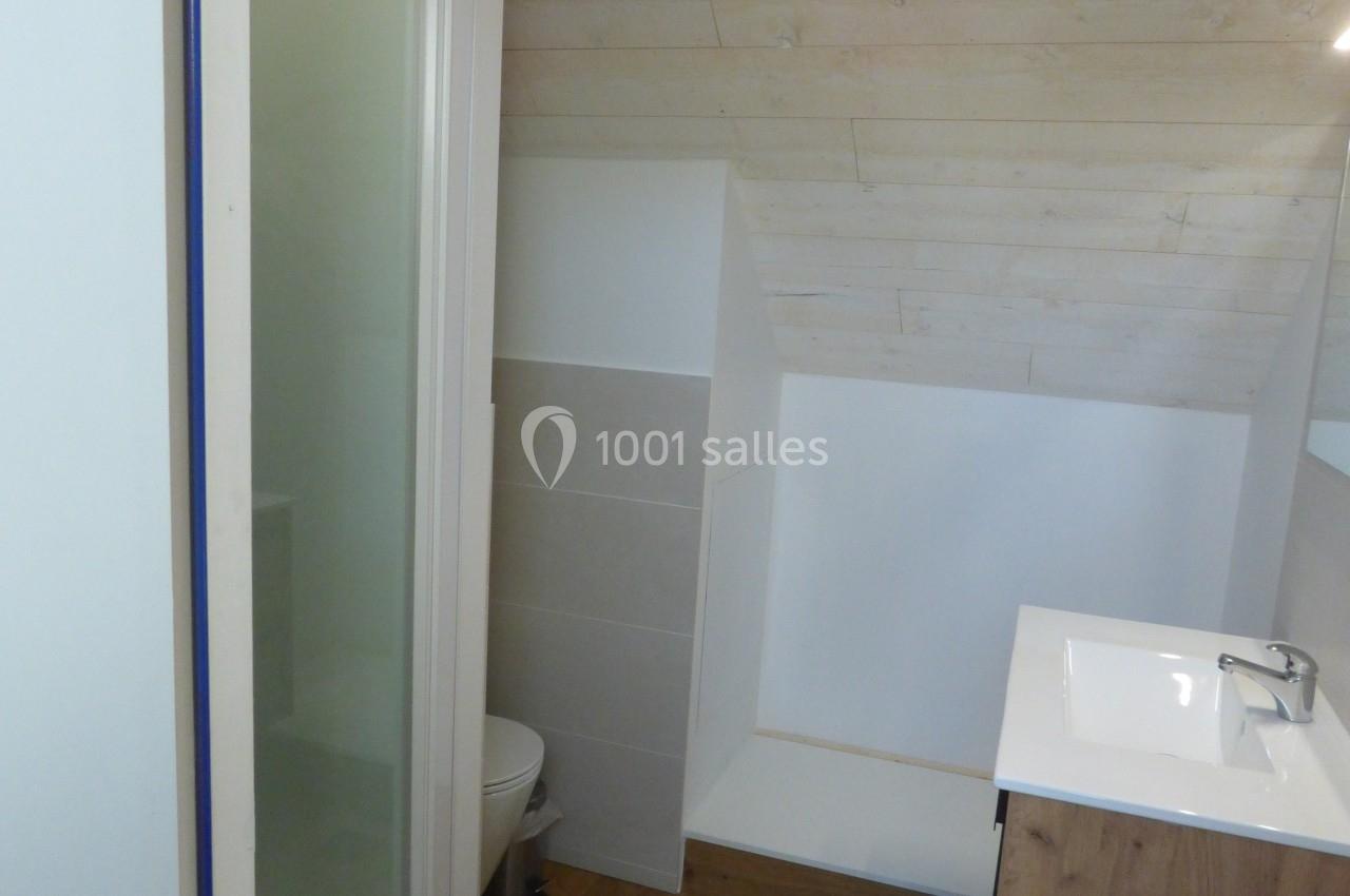 Salle de bain mansardée avec douche, lavabo sur meuble en bois, toilettes et sol en parquet.