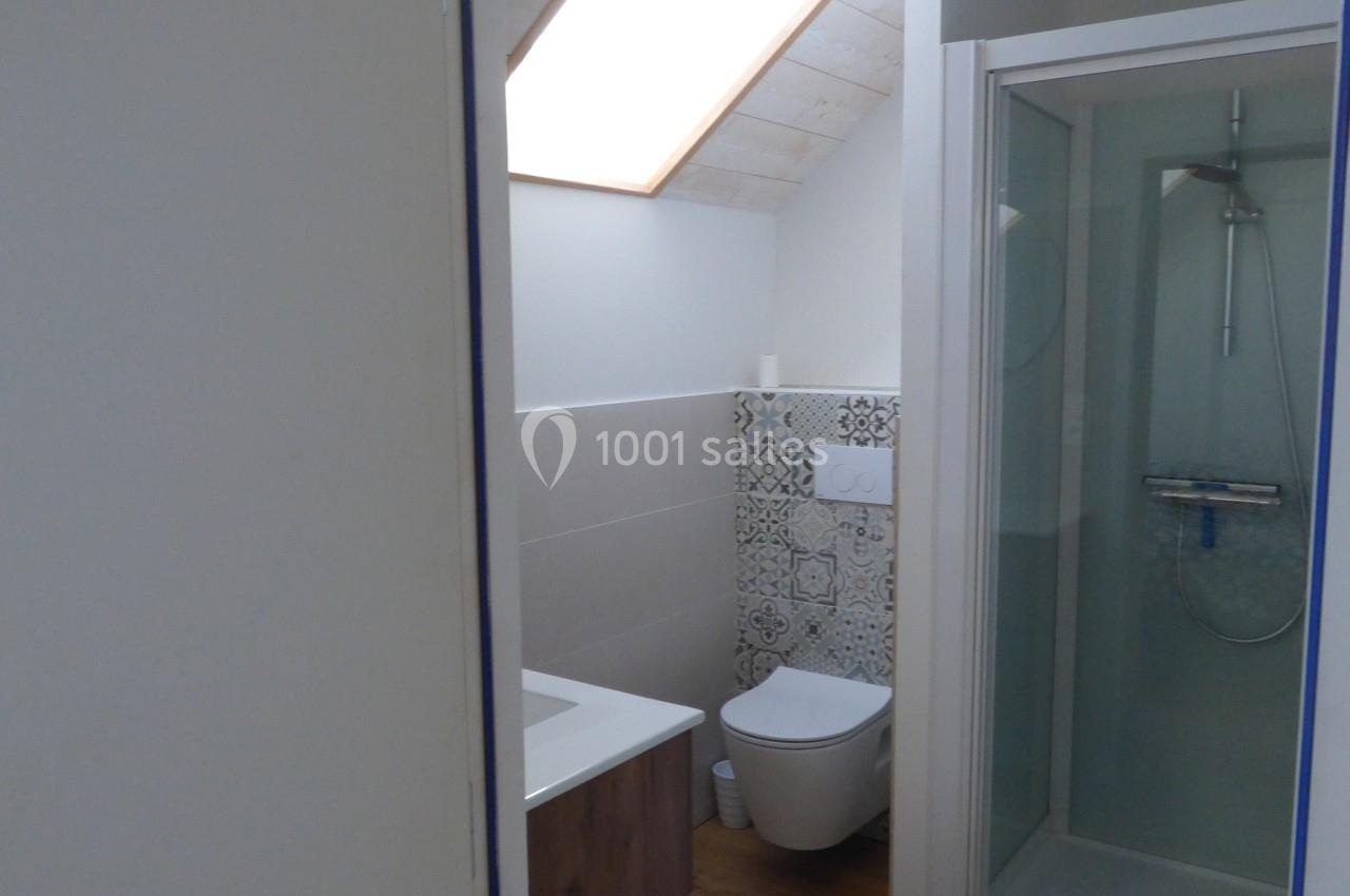 Salle de bain avec douche vitrée, toilettes, lavabo en bois et fenêtre de toit apportant de la lumière naturelle.