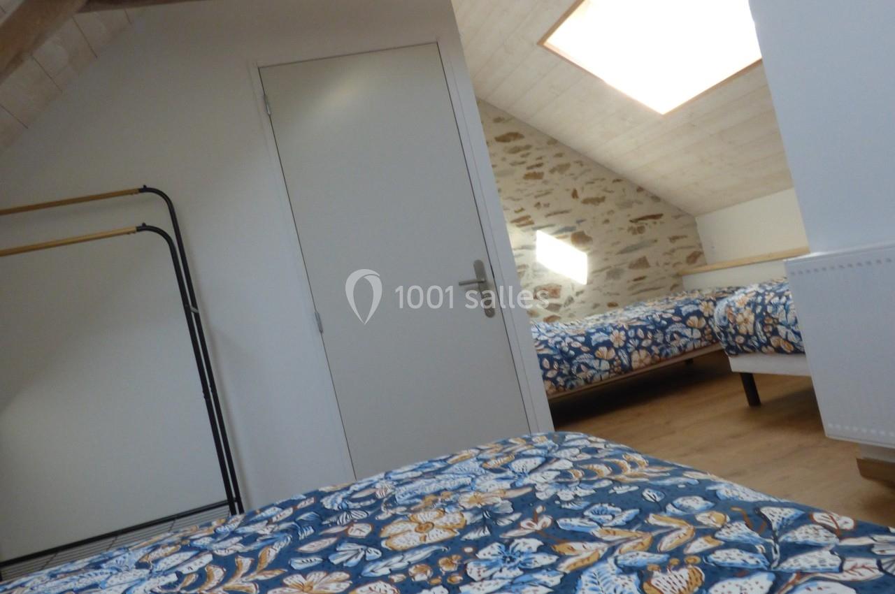 Chambre mansardée avec poutres apparentes, deux lits aux motifs floraux et lumière naturelle provenant d'un velux.