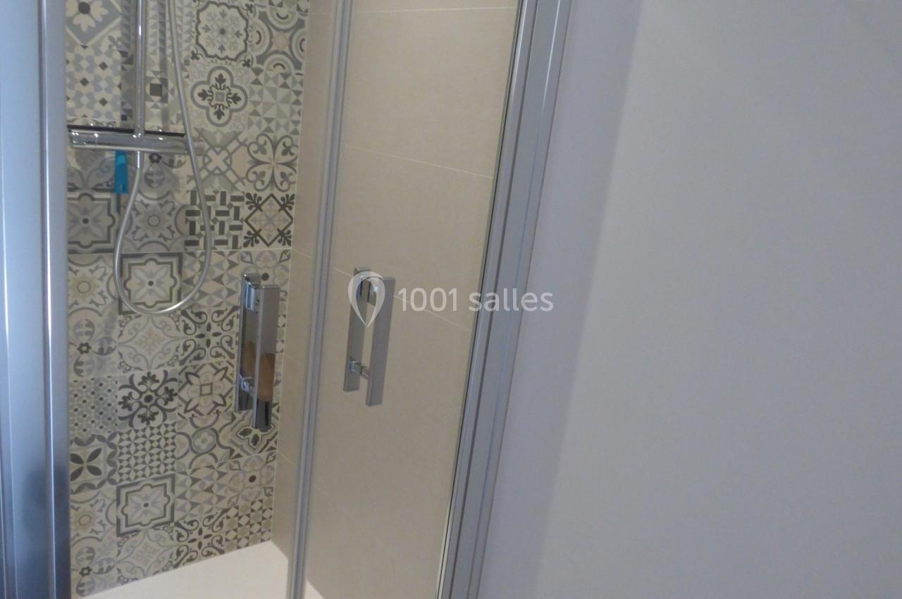 Douche avec paroi vitrée, carrelage à motifs géométriques et sol blanc, située dans une salle de bain.