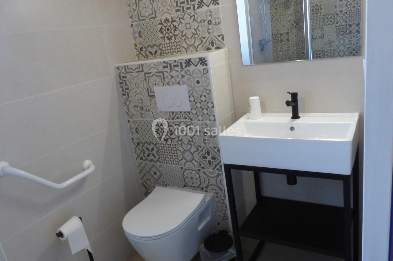 Salle de bain avec toilettes, lavabo sur meuble noir, carrelage décoratif et barre d'appui murale.