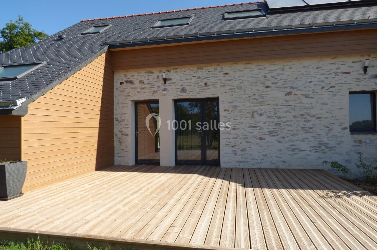 Terrasse en bois devant une maison moderne avec façade en pierre et bardage en bois, équipée de panneaux solaires.