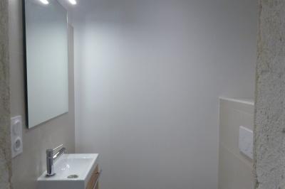 Allée bordée de végétation dense avec un château gonflable coloré visible à gauche et des bâtiments en arrière-plan.