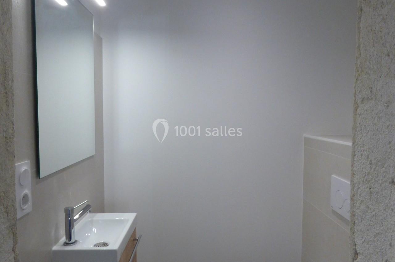 Salle de bain compacte avec lavabo en bois, miroir éclairé, toilettes blanches et carrelage à motifs au sol.