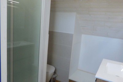 Allée bordée de végétation dense avec un château gonflable coloré visible à gauche et des bâtiments en arrière-plan.