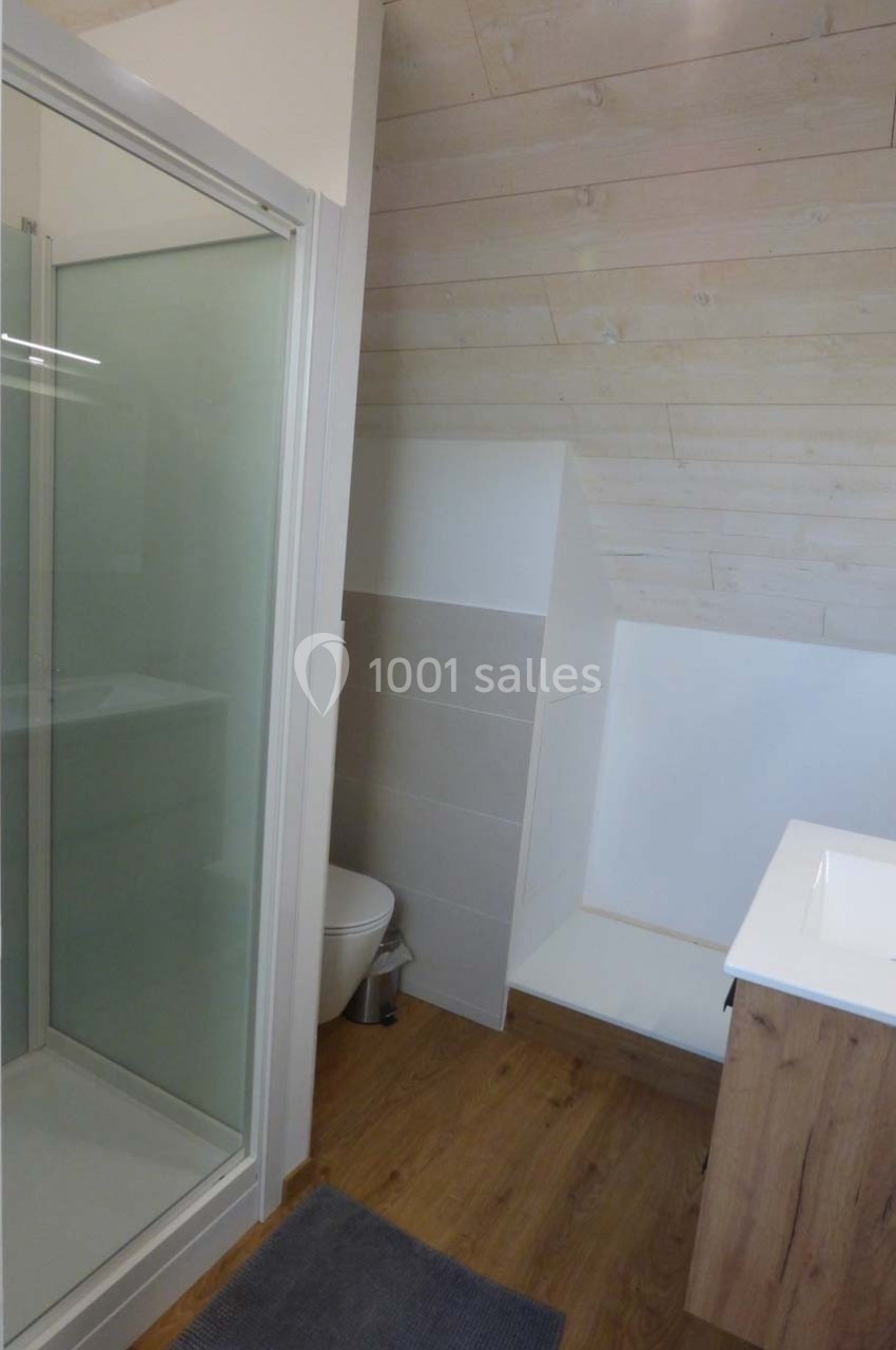 Salle de bain mansardée avec douche vitrée, lavabo sur meuble en bois et sol en parquet clair.