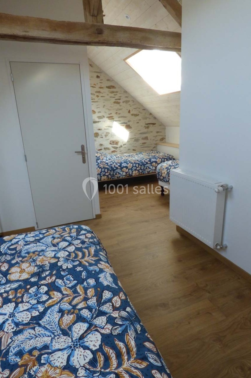 Chambre mansardée avec deux lits simples, parquet en bois, murs en pierre et plafond avec poutres apparentes.