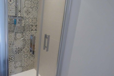 Allée bordée de végétation dense avec un château gonflable coloré visible à gauche et des bâtiments en arrière-plan.