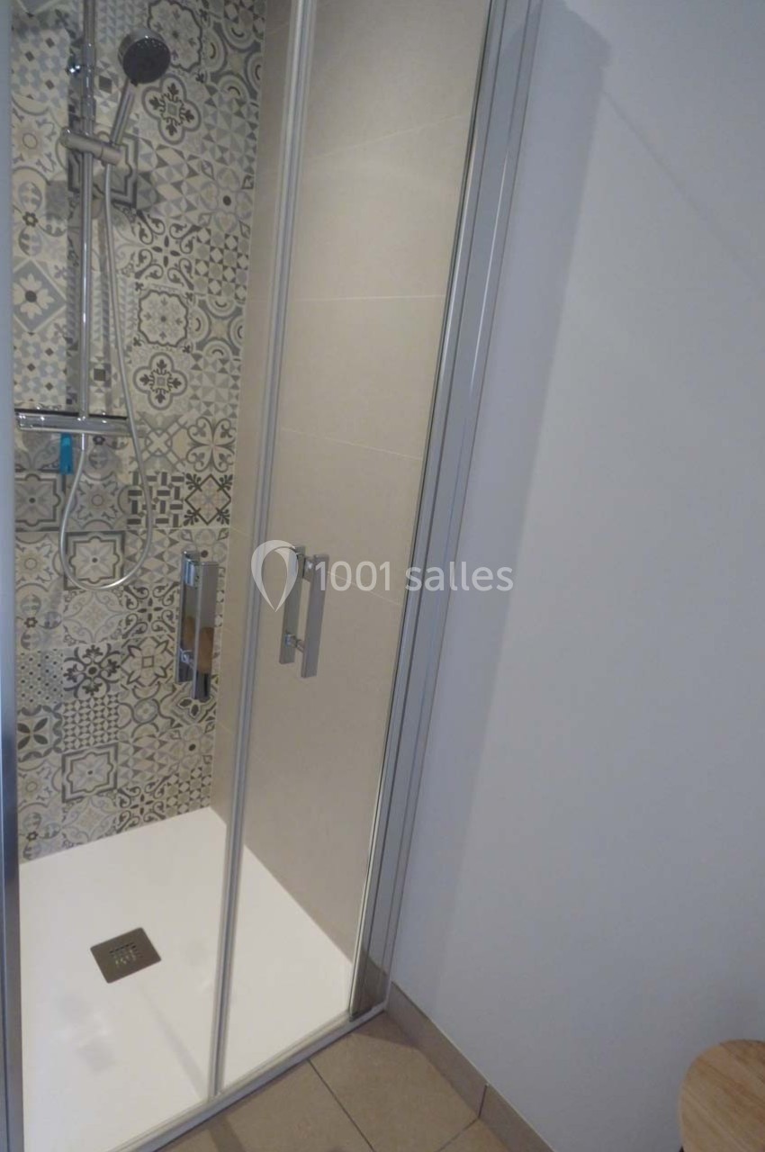 Douche moderne avec paroi vitrée, carrelage à motifs géométriques et pommeau de douche mural.