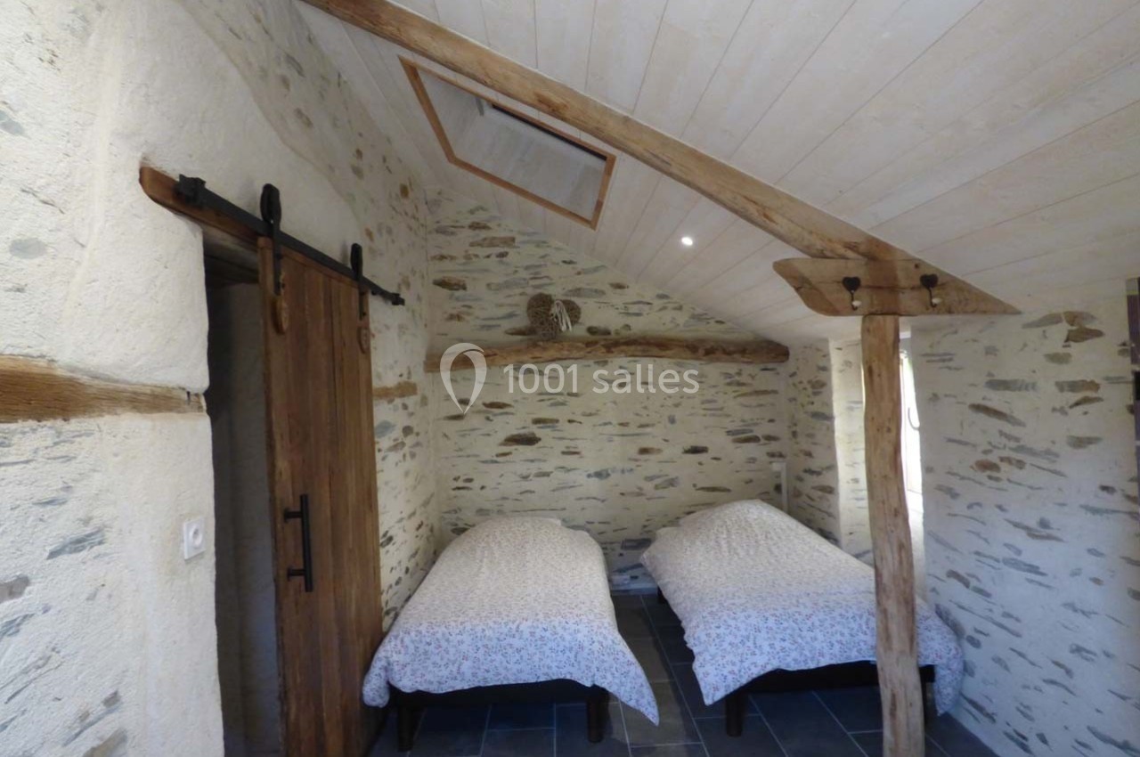 Chambre avec deux lits simples, murs en pierre apparente, poutres en bois et porte coulissante rustique.
