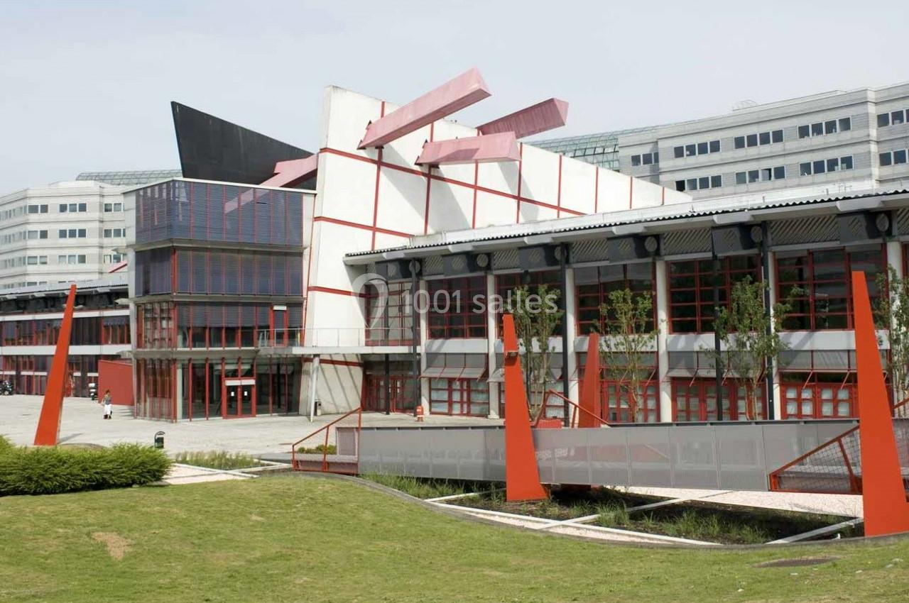 Bâtiment moderne avec une architecture géométrique, des structures rouges et des espaces verts au premier plan.