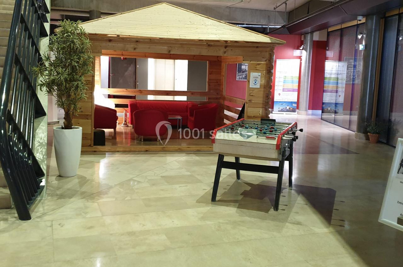 Espace détente intérieur avec une cabane en bois, des fauteuils rouges, un baby-foot et un escalier à gauche.