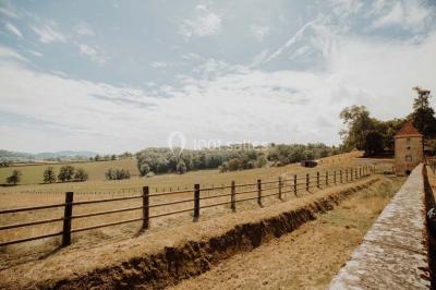 Paysage rural avec une clôture en bois, des champs verdoyants, des arbres et un bâtiment en pierre sous un ciel…