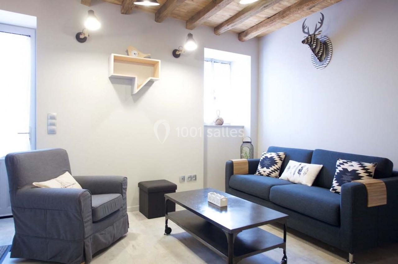 Salon lumineux avec canapé bleu, fauteuil gris, table basse en métal et bois, étagère murale et décoration murale de cerf.