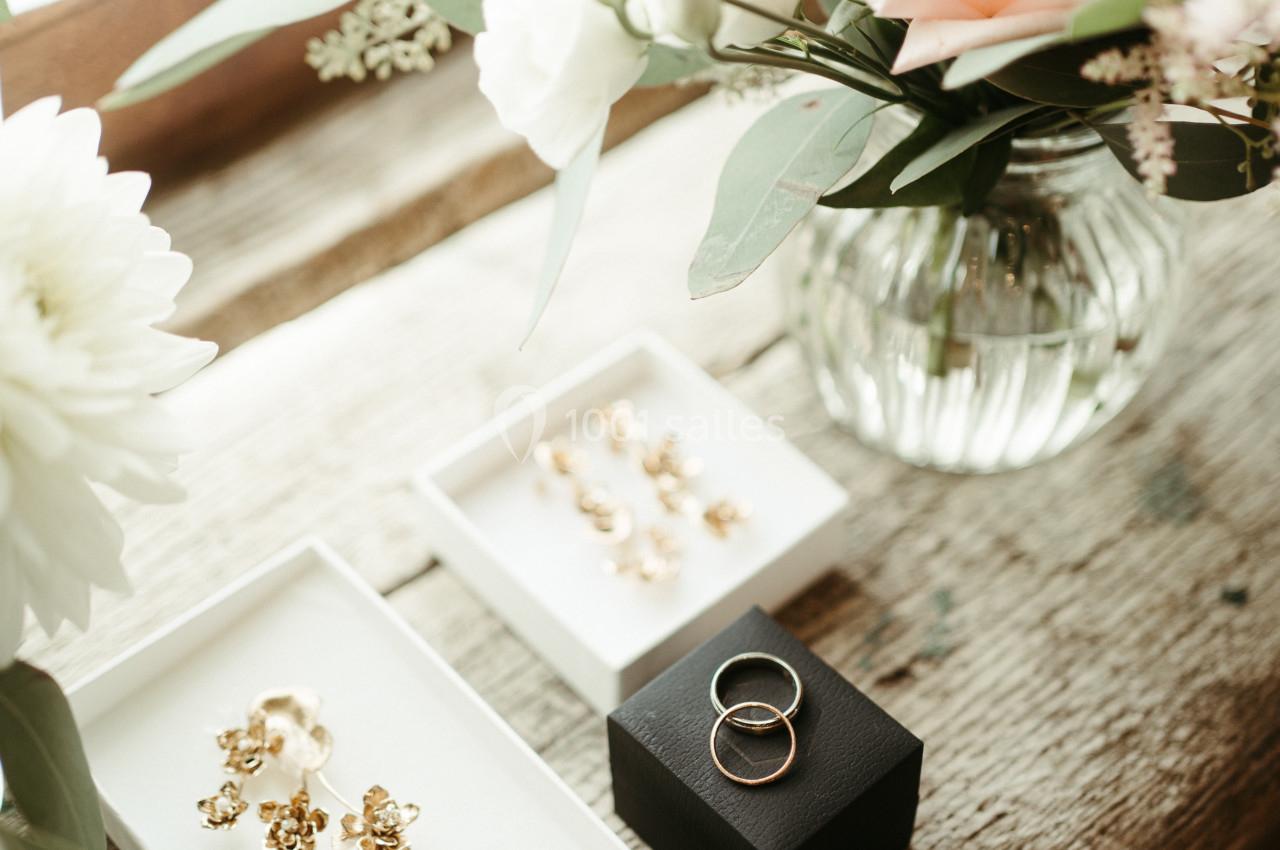 Boucles d'oreilles dorées et alliances posées sur une table en bois près d'un vase de fleurs.