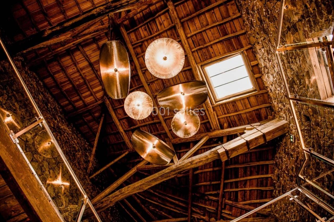 Plafond en bois avec poutres apparentes, éclairé par des suspensions lumineuses modernes et une fenêtre.