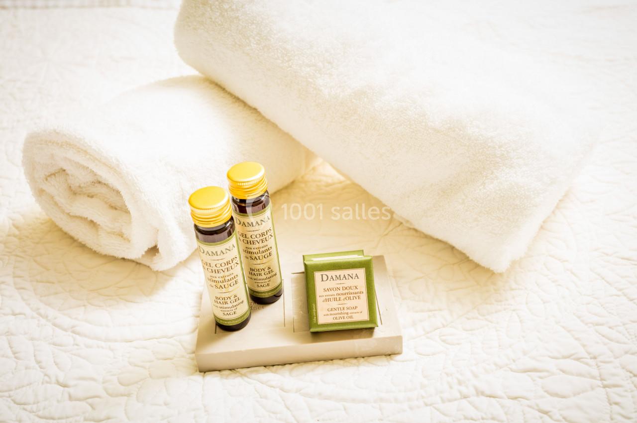 Deux serviettes blanches roulées avec des produits de toilette disposés sur un plateau en bois.