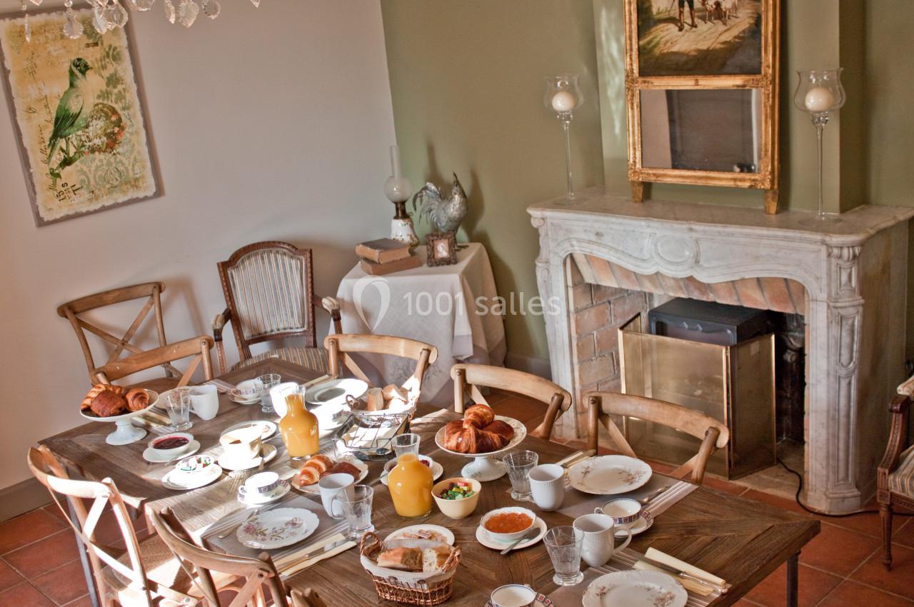 Table dressée pour un petit-déjeuner avec viennoiseries, jus d'orange et vaisselle, dans une salle à manger lumineuse.