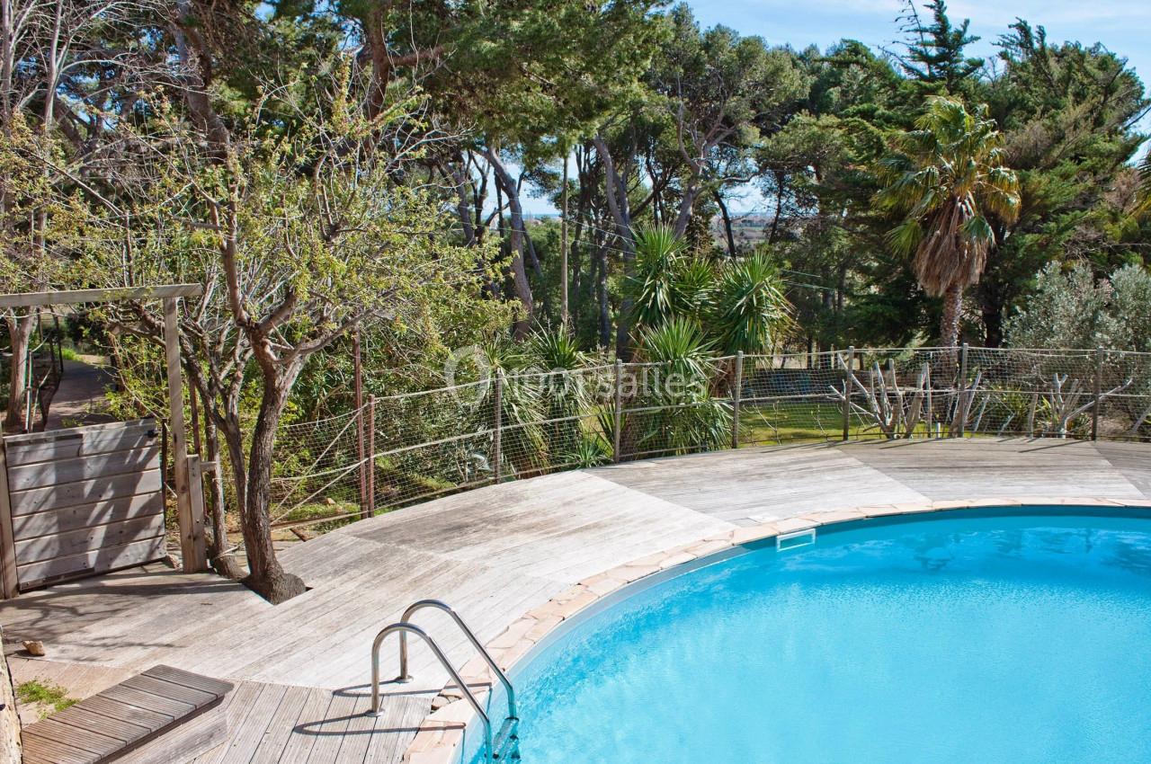 Piscine extérieure entourée d'une terrasse en bois et de végétation dense avec des arbres et des palmiers.