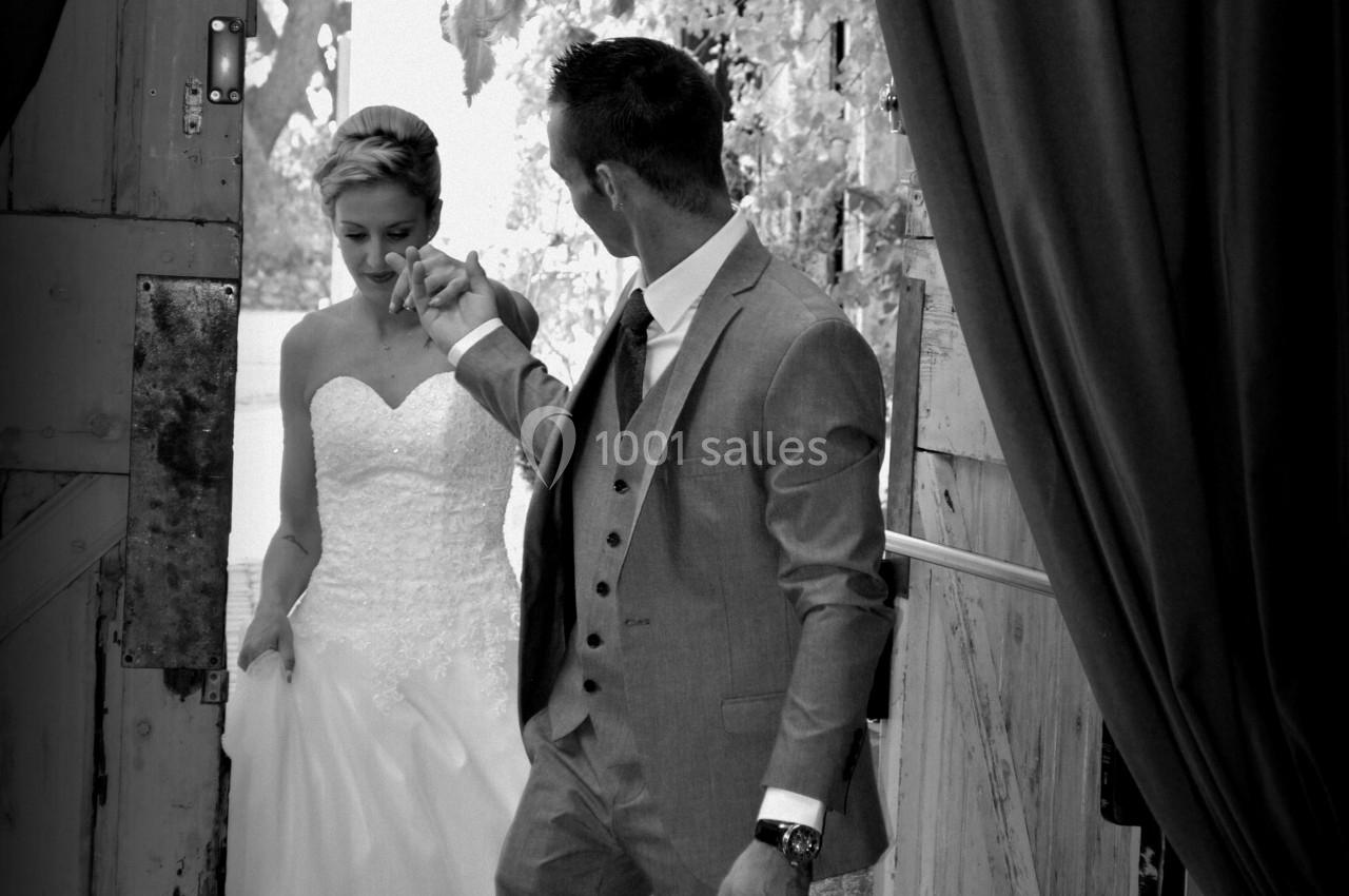 Un couple en tenue de mariage entre par une porte en bois, entouré de décorations florales.