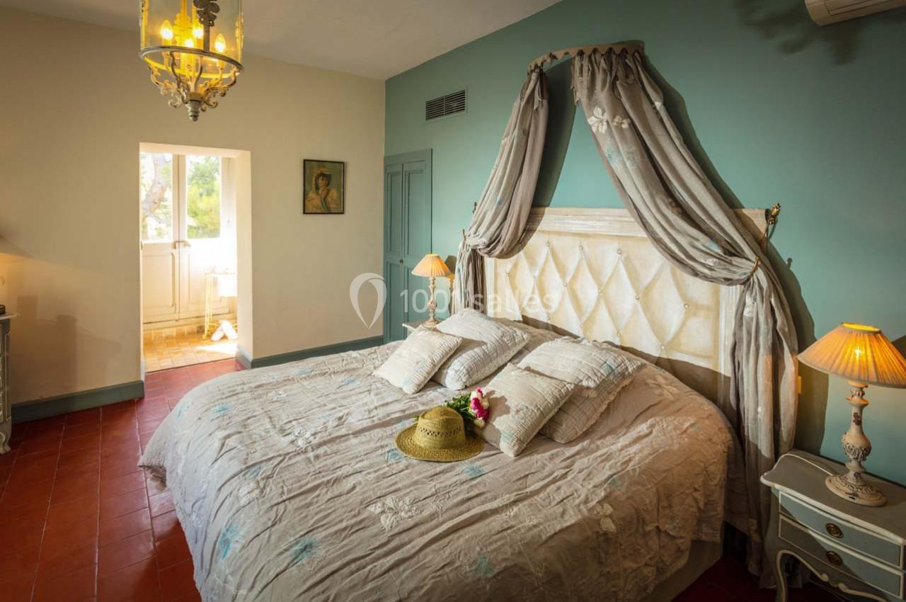 Chambre lumineuse avec lit double, baldaquin, lampes de chevet et vue sur une porte donnant sur l'extérieur.