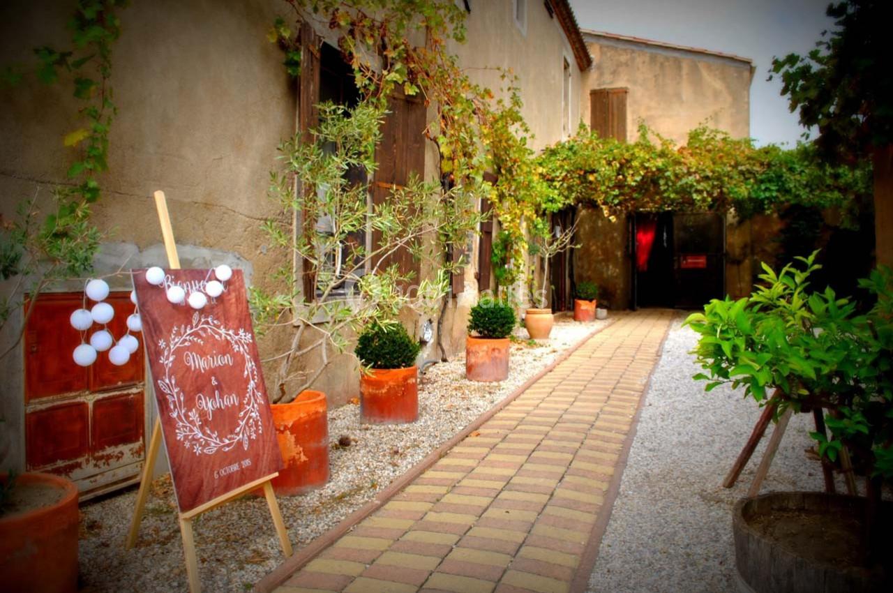 Allée pavée bordée de plantes menant à une entrée, avec un panneau décoratif en bois sur la gauche.