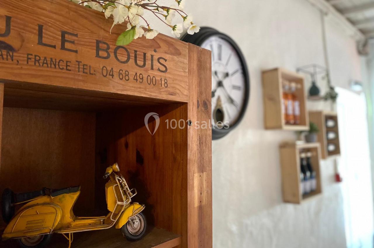 Étagère en bois avec une miniature de scooter jaune, fleurs décoratives et mur blanc orné de cadres et d'une horloge.