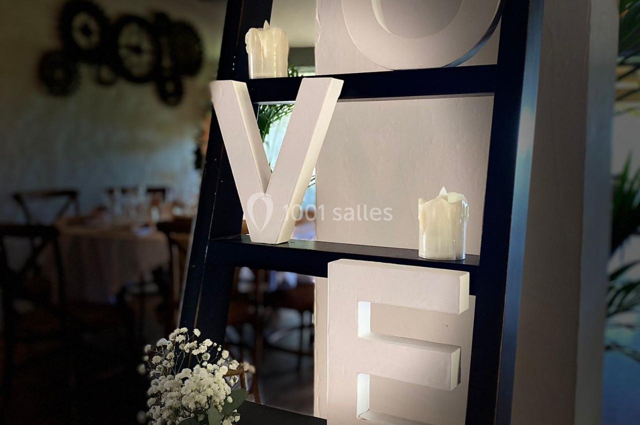 Étagère noire décorative avec le mot ’LOVE’ en lettres blanches, bougies et vase de fleurs blanches au premier plan.