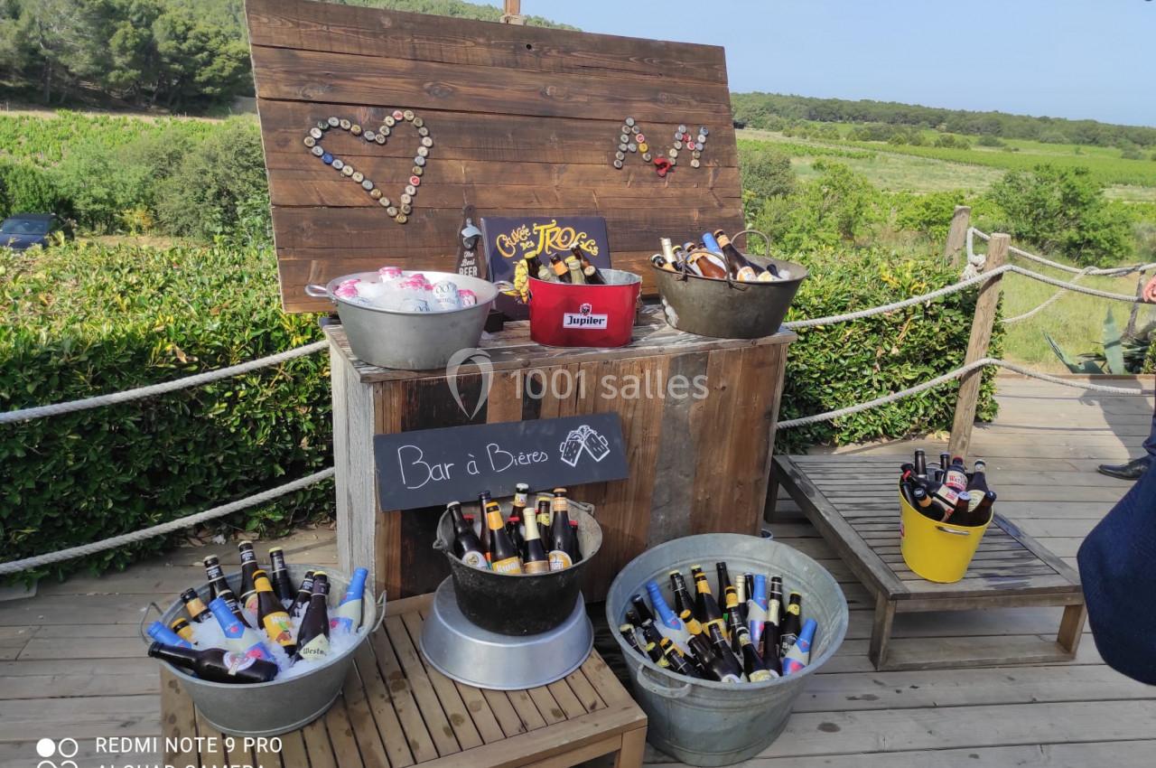 Bar extérieur avec seaux remplis de bouteilles de bière et de glace, décoré de bois et entouré de verdure.