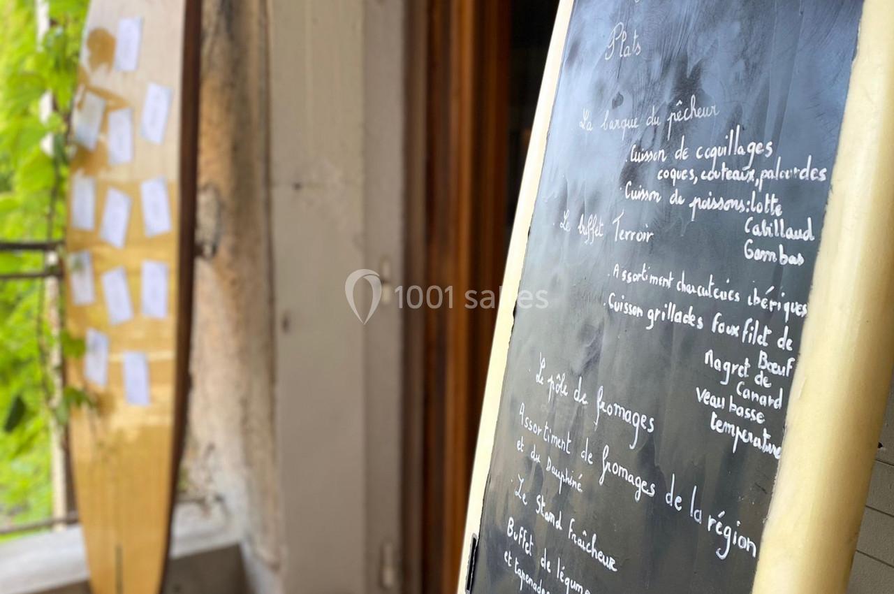 Ardoise avec menu écrit à la craie, posée devant l'entrée d'un restaurant avec une planche de surf en arrière-plan.