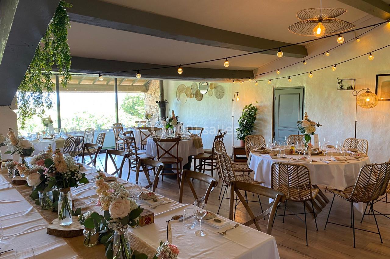 Salle de réception décorée avec des tables dressées, des fleurs et des guirlandes lumineuses, offrant une vue sur l…
