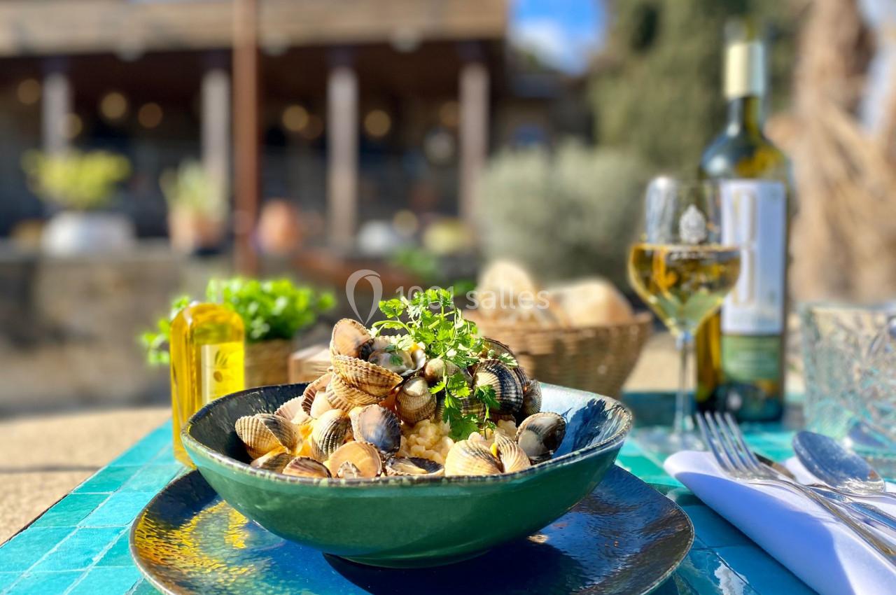 Assiette de fruits de mer avec herbes fraîches, servie en extérieur sur une table turquoise avec vin et pain en arrière-plan.