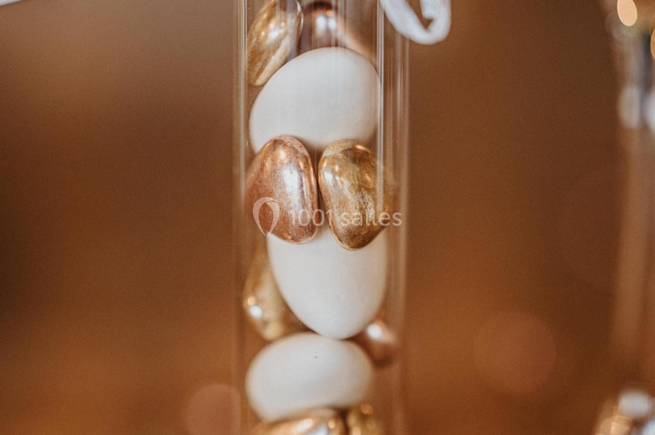 Tube en verre avec bouchon en liège contenant des dragées blanches et dorées, posé sur une table.