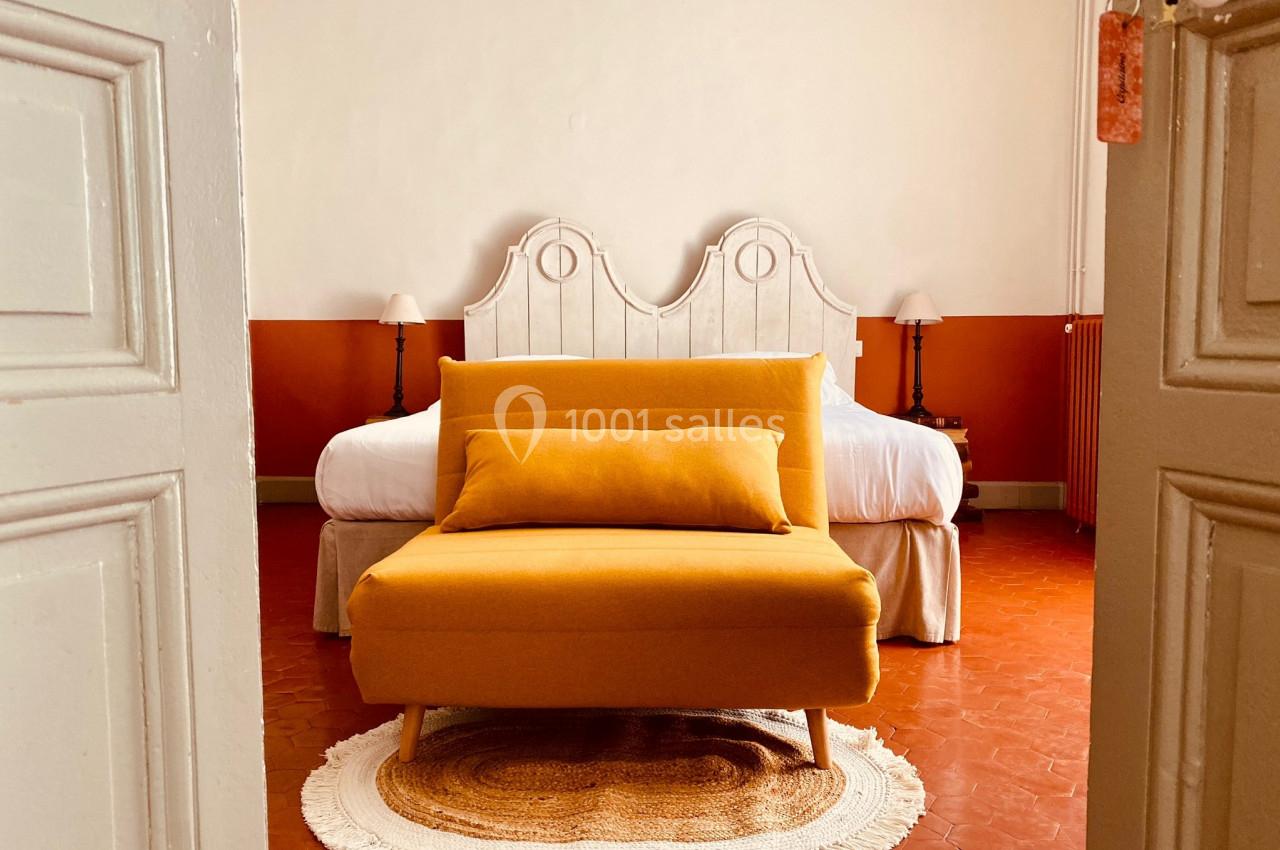 Fauteuil jaune devant un lit à tête de lit blanche, posé sur un tapis rond dans une chambre aux murs bicolores.