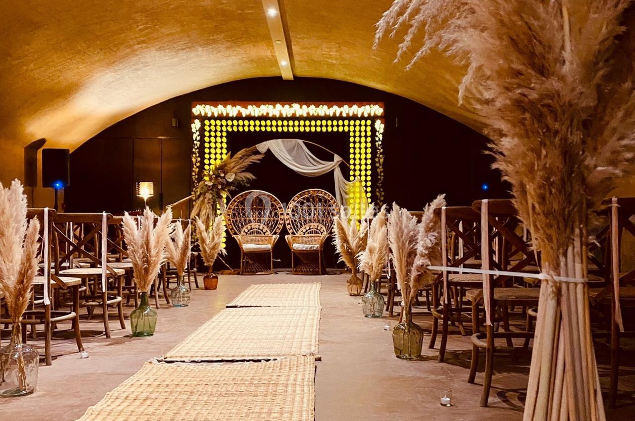 Allée décorée de tapis et de pampas menant à une arche lumineuse dans une salle voûtée.