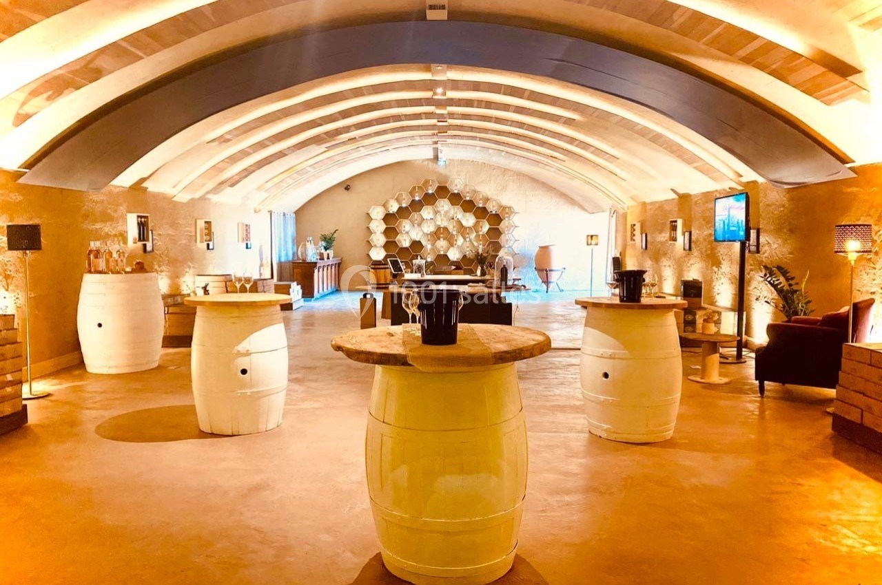 Salle voûtée lumineuse avec des tonneaux utilisés comme tables, décorée de murs en pierre et d'éléments modernes.