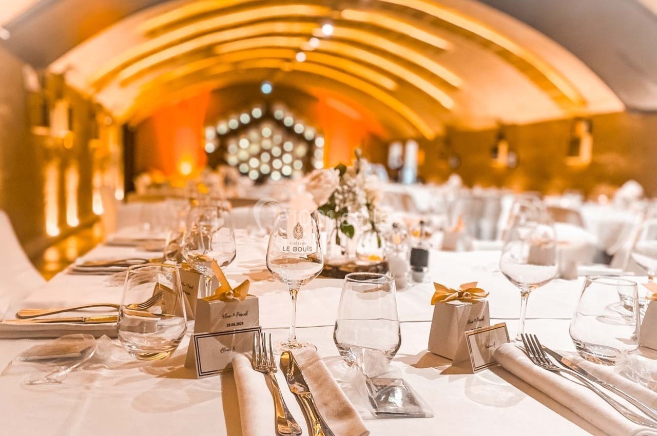 Salle de réception élégante avec tables dressées, décorations raffinées et éclairage chaleureux sous un plafond voûté.