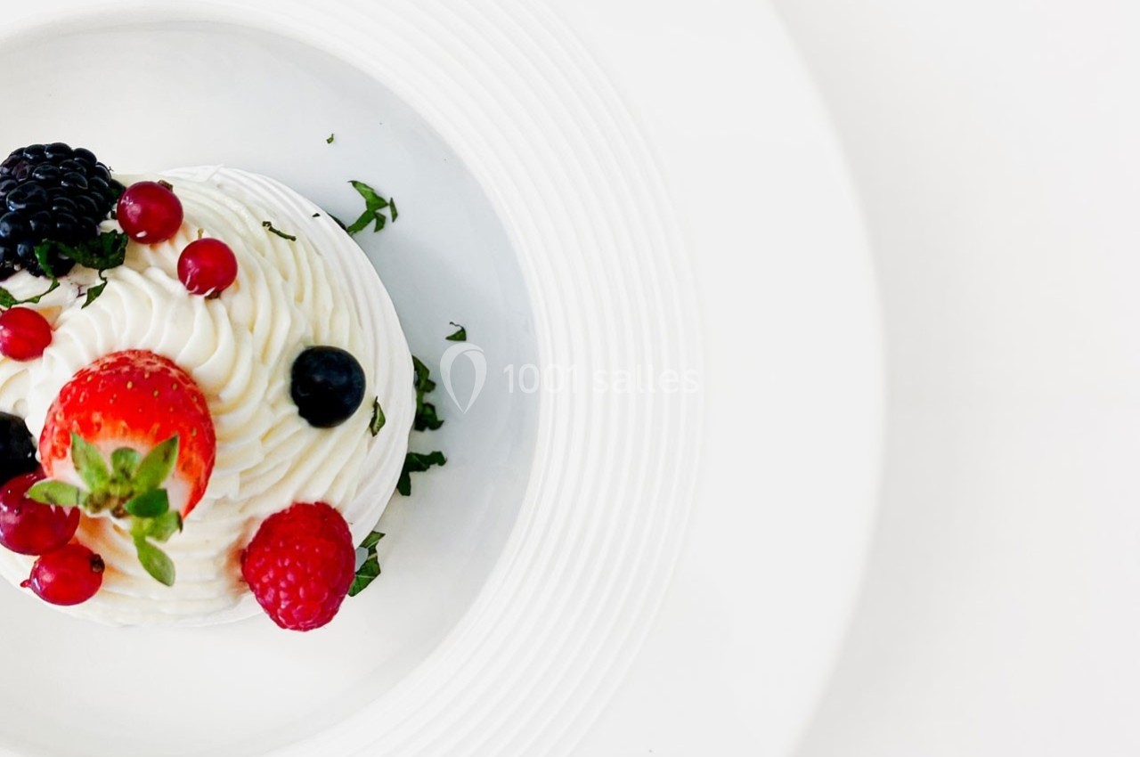Dessert à base de crème fouettée, garni de fraises, framboises, myrtilles, mûres et groseilles, sur une assiette blanche.