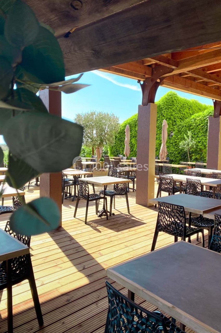 Terrasse extérieure avec tables et chaises modernes, ombragée par une pergola en bois, entourée de verdure.