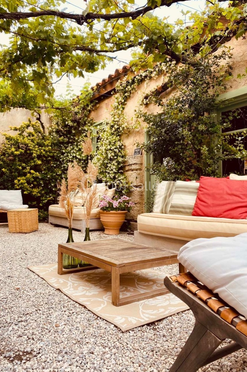 Cour extérieure avec mobilier de jardin, coussins colorés, table basse en bois et plantes grimpantes sur les murs.