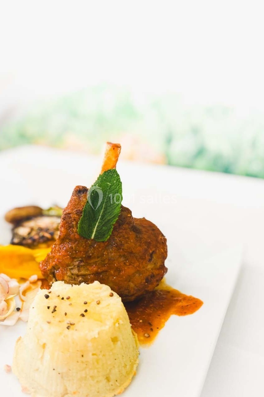 Assiette composée d'un jarret d'agneau en sauce, accompagné de purée, légumes et décorée d'une feuille de menthe.