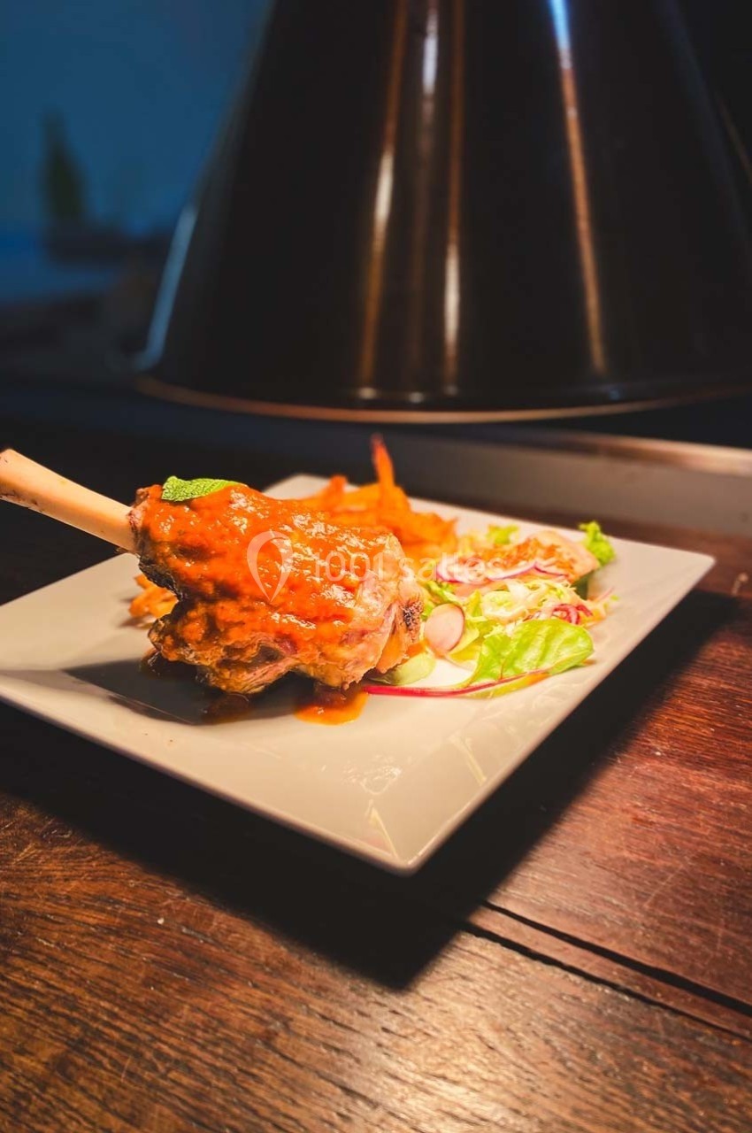 Plat de jarret d'agneau nappé de sauce rouge, accompagné de légumes frais et servi sur une assiette blanche.