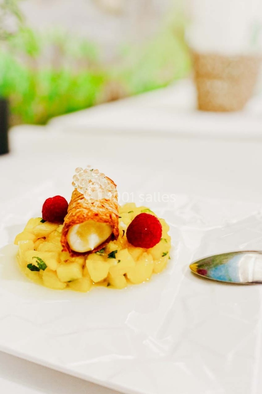 Dessert composé d'un cannolo garni, entouré de dés de fruits frais, décoré de framboises et de perles translucides.