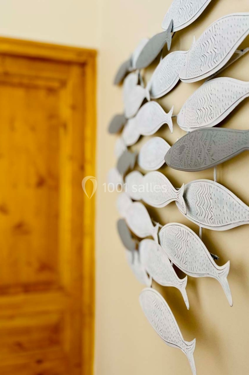 Décoration murale composée de poissons blancs et gris alignés, avec une porte en bois en arrière-plan.