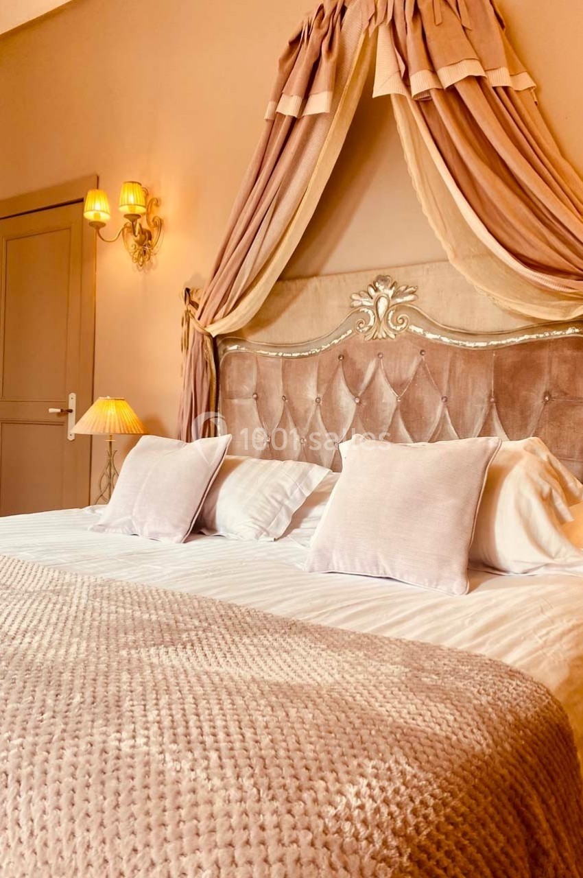 Lit double avec tête de lit capitonnée, baldaquin en tissu rose et éclairage doux dans une chambre élégante.