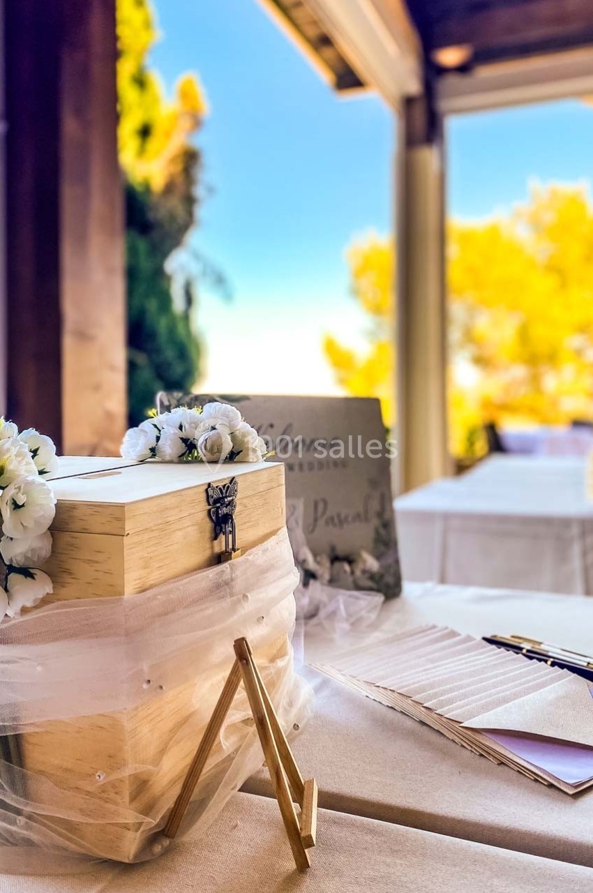 Boîte en bois décorée pour un mariage, entourée de fleurs blanches, sur une table avec des stylos et des cartes.