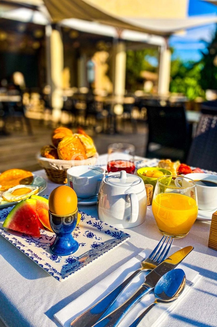 Petit-déjeuner en terrasse avec œuf à la coque, fruits, viennoiseries, jus d'orange et thé sur une table dressée.
