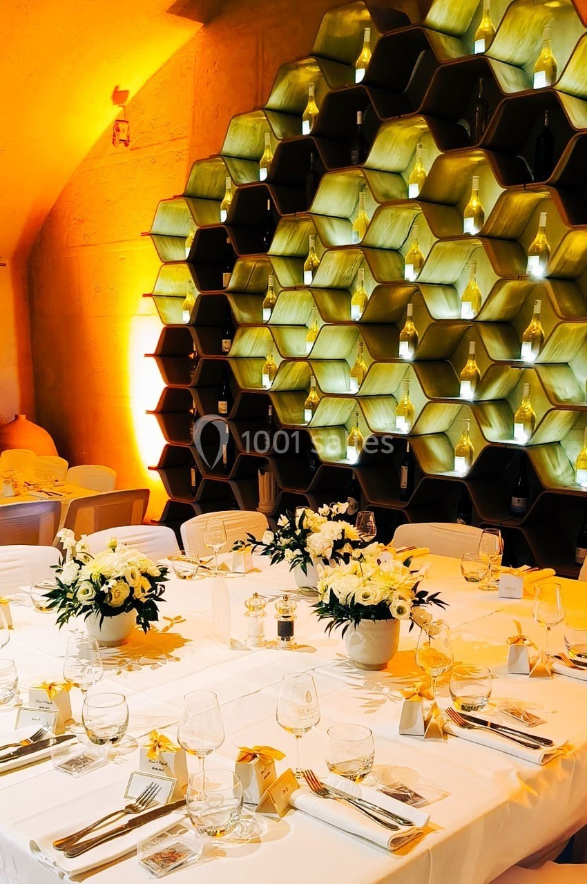 Tables élégamment dressées avec des fleurs blanches devant un mur décoratif en forme de rayons de miel illuminés.